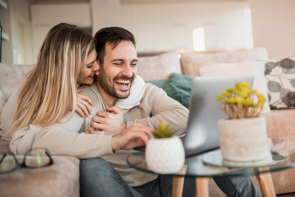 Young,Couple,Relaxing,On,Sofa,With,Laptop.love,happiness,people,And,Fun,Concept.